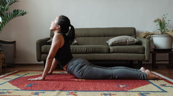 a woman practicing cobra pose or bhujangasana yoga at home. It stretches the chest cavity, shoulders and abdomen. Also strengthens the spine