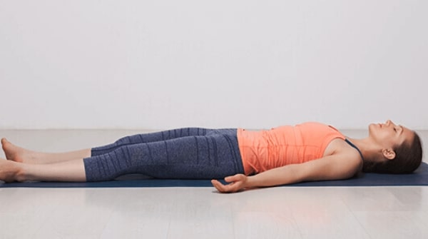 a woman is doing the Corpse pose also known as savasana to end her yoga session. Helps in overall relaxation of the body