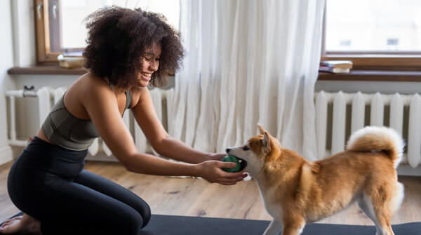 a woman playing with her dog while practicing yoga at home