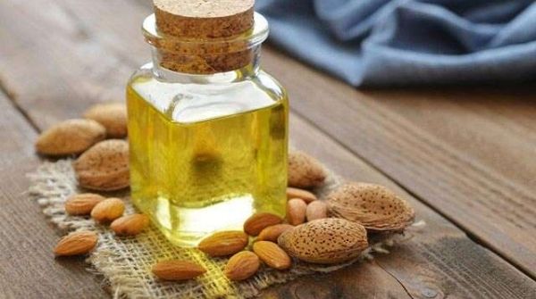 A flask of sweet almond massage oil surrounded by some almonds.