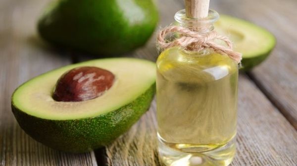 a flask of avocado massage oil with some some avocados near it.
