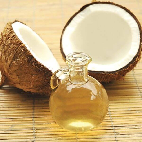 A flask of coconut massage oil with two halves of coconut.