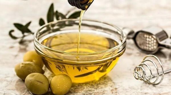 A bowl of olive massage oil with some olives around it.